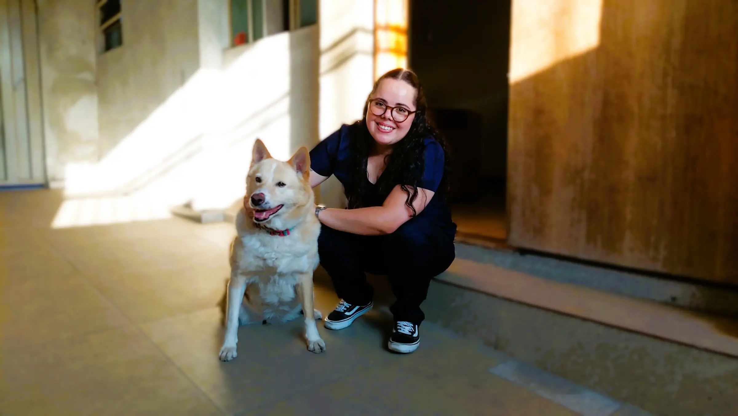 Dra. Nathalia Helen agachada ao lado de um cão na entrada de uma casa